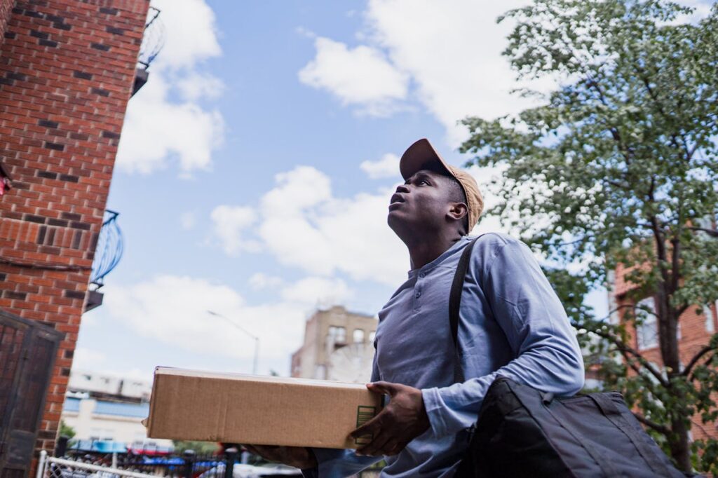 Man delivering a package in a city neighborhood, looking up at the building.